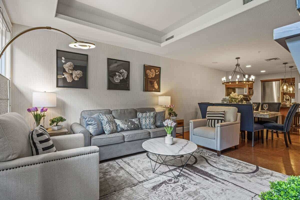 A modern living room with a grey sofa, a round coffee table, and a dining area with a chandelier.