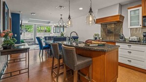 A modern kitchen with a central island, bar stools, pendant lighting, and a stone fireplace. - NEW!The Louvre by SSR Top Luxury|1000SQF|2BR&2BTH ( BL# RES-11739 ) (Canmore)