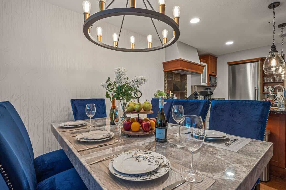 A dining area with a marble table, blue upholstered chairs, a chandelier, and a fruit display.