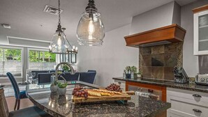 A modern kitchen with granite countertops, a central island with a fruit platter, pendant lighting, and a view of the outdoors. - NEW!The Louvre by SSR Top Luxury|1000SQF|2BR&2BTH ( BL# RES-11739 ) (Canmore)