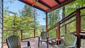 Een houten terras met Adirondack-stoelen en uitzicht op een bos.