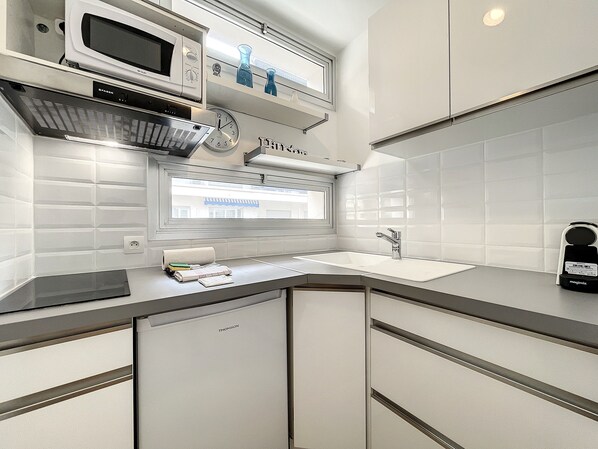A modern kitchen with white tiles, a built-in microwave, a sink, and a window with a view of a building.