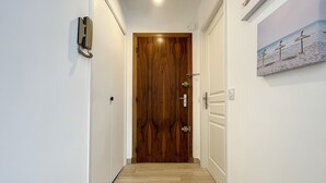 Un couloir avec une porte en bois, un interrupteur et un tableau accroché au mur.