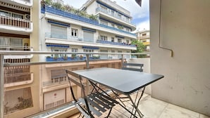 Un balcon avec une table et des chaises, donnant sur un immeuble doté de nombreux balcons et fenêtres.