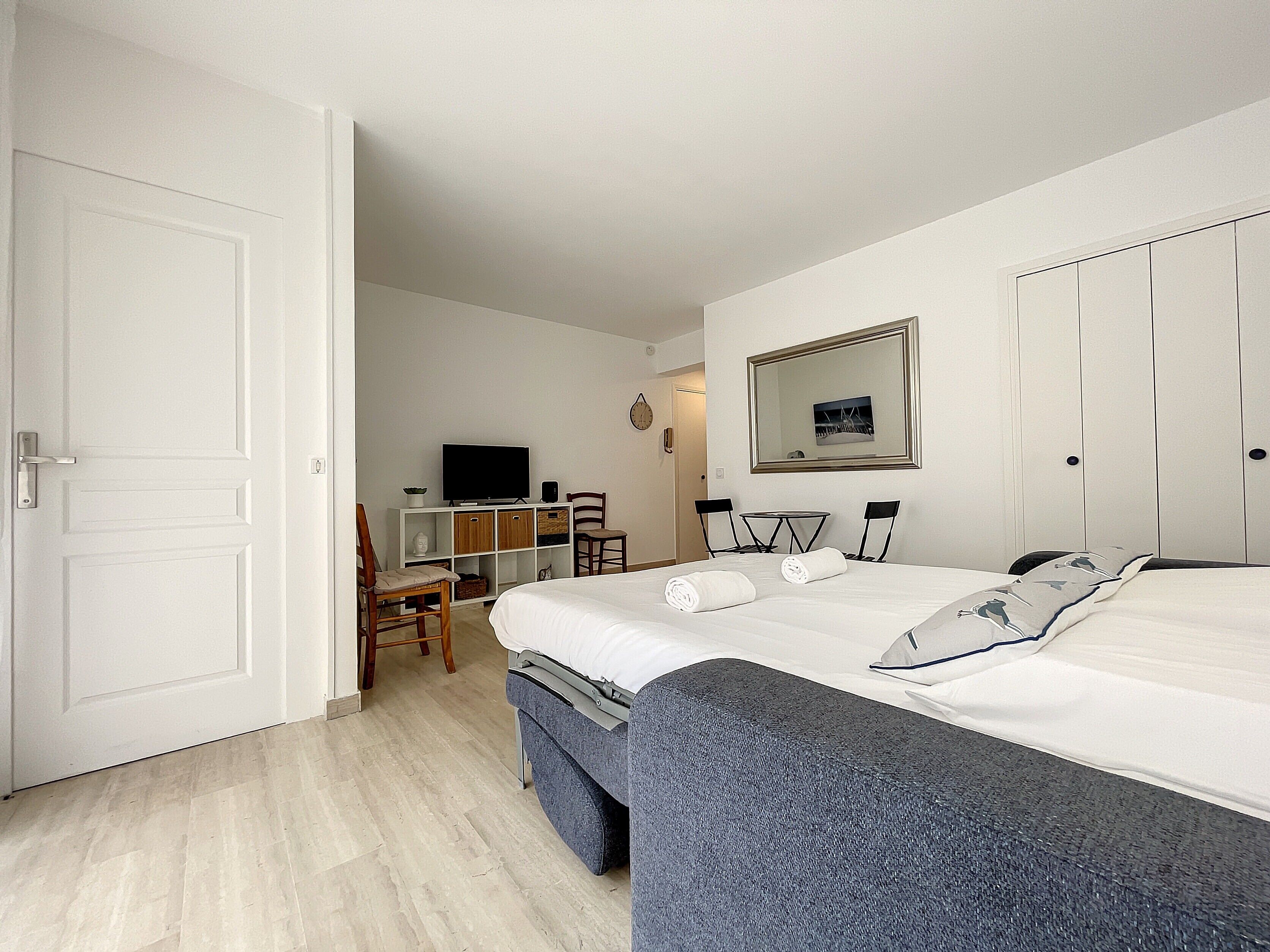 A hotel room with a bed, a desk with a TV, a chair, and a wardrobe.