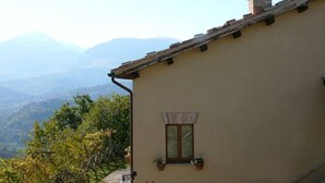 A building with a beige exterior, a window with a curtain, and two chimneys on the roof. - Cottage with breathtaking views of the Sibillini Mountains (Marche)