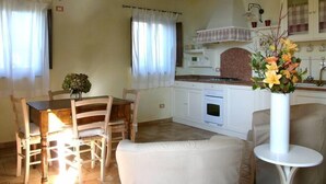 A cozy kitchen with a dining area, featuring a table with chairs, a vase with flowers, and a white cabinet with a stove. - Cottage with breathtaking views of the Sibillini Mountains (Marche)