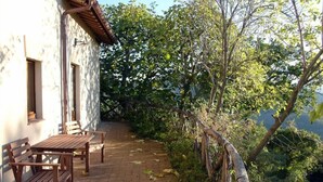 A patio with a table and chairs, a stone wall, and a view of trees and a fence. - Cottage with breathtaking views of the Sibillini Mountains (Marche)
