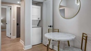Quarto com mesa de mármore branco, cadeiras douradas, espelho redondo e eletrodoméstico embutido branco.