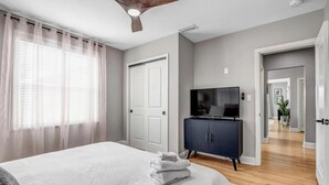 A bedroom with a bed, a TV, a dark cabinet, and a ceiling fan.