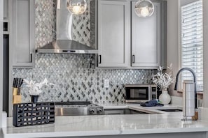 A modern kitchen with grey cabinets, a stainless steel range hood, a microwave, and a sink.