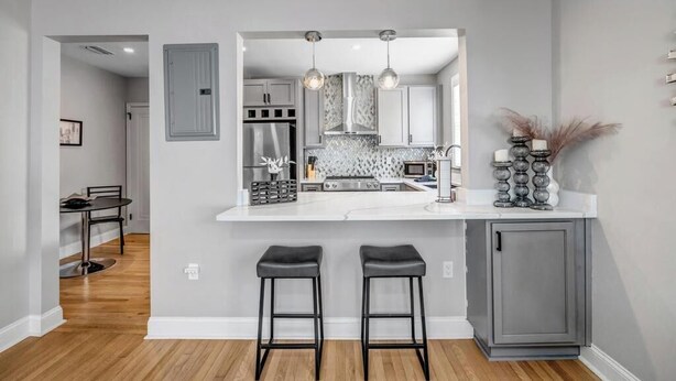 A modern kitchen with a white countertop, two bar stools, and a gray cabinet.