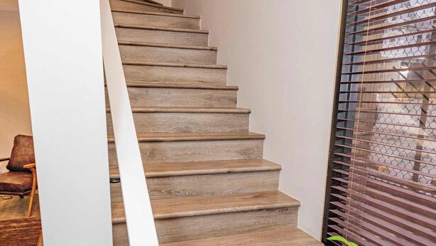 A wooden staircase with a white handrail, leading to a room with a window and a plant.