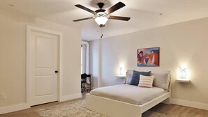 Un dormitorio con una cama, ventilador de techo, un cuadro y dos lámparas de pared.
