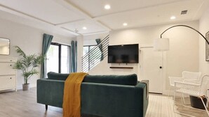 Una sala de estar moderna con un sofá verde, un televisor de pantalla plana, una escalera y una silla blanca.