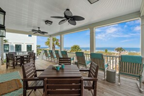 A covered outdoor deck with a wooden table and chairs, a ceiling fan, and a view of the ocean. - The Pressian: Oceanfront, Pool & Hot Tub (Garden City Beach)