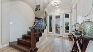 Un escalier en bois menant à une porte dotée de panneaux de verre, un luminaire au-dessus et un vase décoratif posé sur une table.
