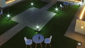 Una terrazza sul tetto con un prato verde, sedie e tavoli bianchi, circondata da un muretto illuminato.