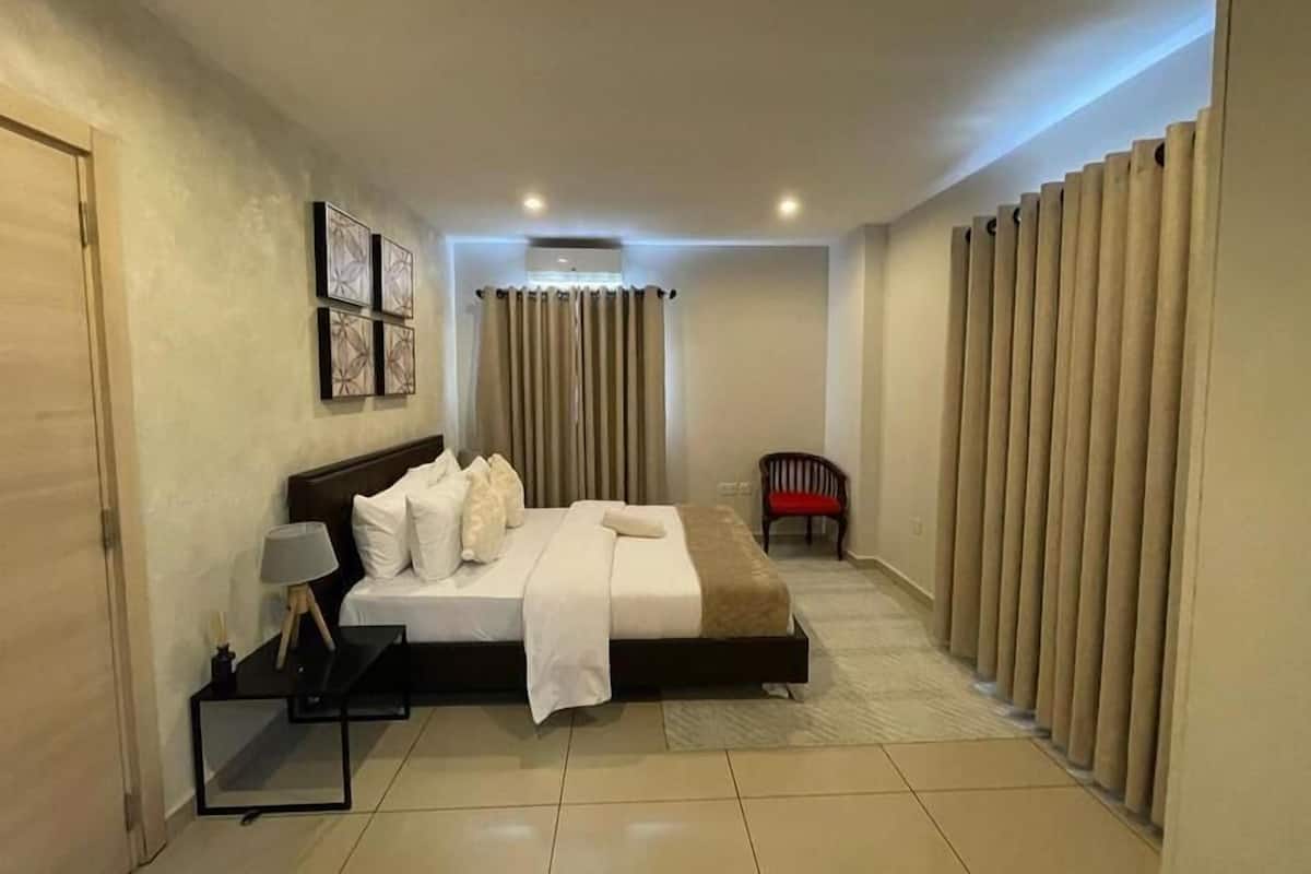 Una habitación de hotel con cama, una silla, una mesita de noche y un espejo.