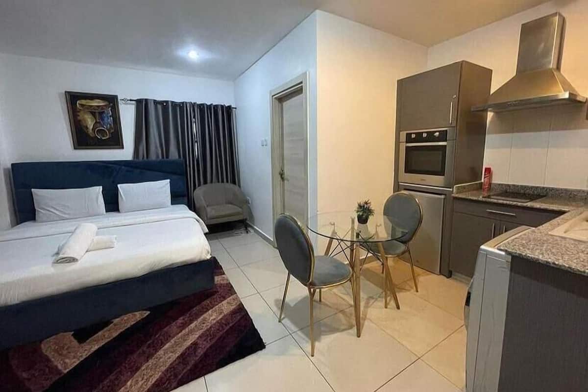 Una habitación de hotel compacta con una cama, un pequeño kitchenette, una mesa de comedor con dos sillas y una butaca.