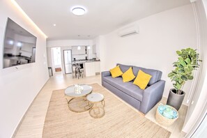 A modern living room with a sofa, two coffee tables, and a potted plant. - Palmas 101: 1BR w Rooftop Pool, 1 Block to Beach (Bucerías)