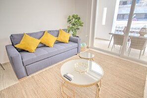 A modern living room with a grey sofa, yellow cushions, a round glass coffee table, and a potted plant. - Palmas 101: 1BR w Rooftop Pool, 1 Block to Beach (Bucerías)