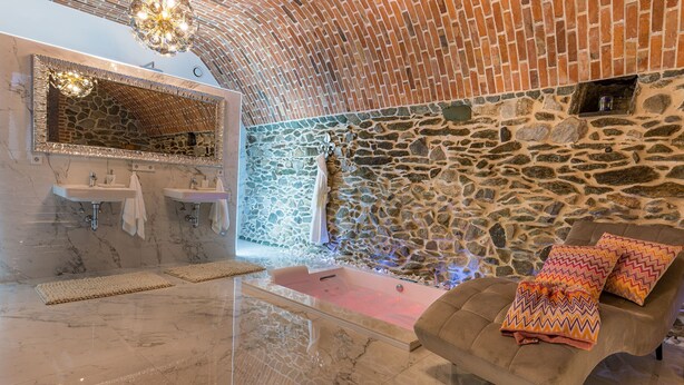 Un baño con pared de piedra, una bañera y un espejo con marco decorativo.