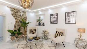 Un salón bien iluminado con una pared de acento de piedra, dos sillones, una mesa de centro y una araña.