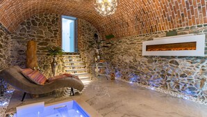 Una habitación de paredes de piedra con un banco curvo, una pequeña piscina y una chimenea.