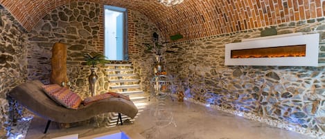 A stone-walled room with a curved bench, a small pool, and a fireplace.