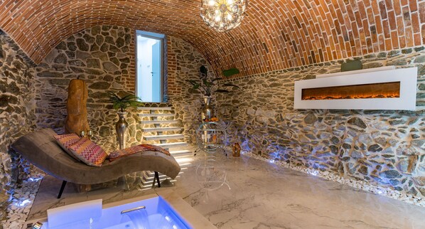 A stone-walled room with a curved bench, a small pool, and a fireplace.