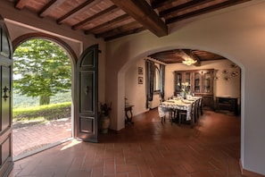 A dining area with a brick floor, wooden beams, and a view of greenery outside.