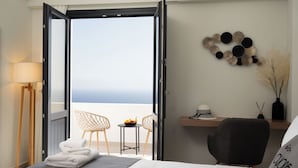 A hotel room with a bed, a desk, a chair, a lamp, and a view of the sea. - CUORE SANTO SUITES  (Santorini)