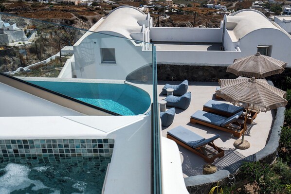A rooftop pool area with lounge chairs and umbrellas, surrounded by white architecture and a view of the landscape. - CUORE SANTO SUITES (Santorini)