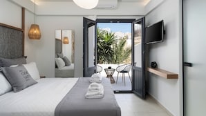 A modern bedroom with a bed, a TV, and a balcony with chairs and plants. - CUORE SANTO SUITES  (Santorini)
