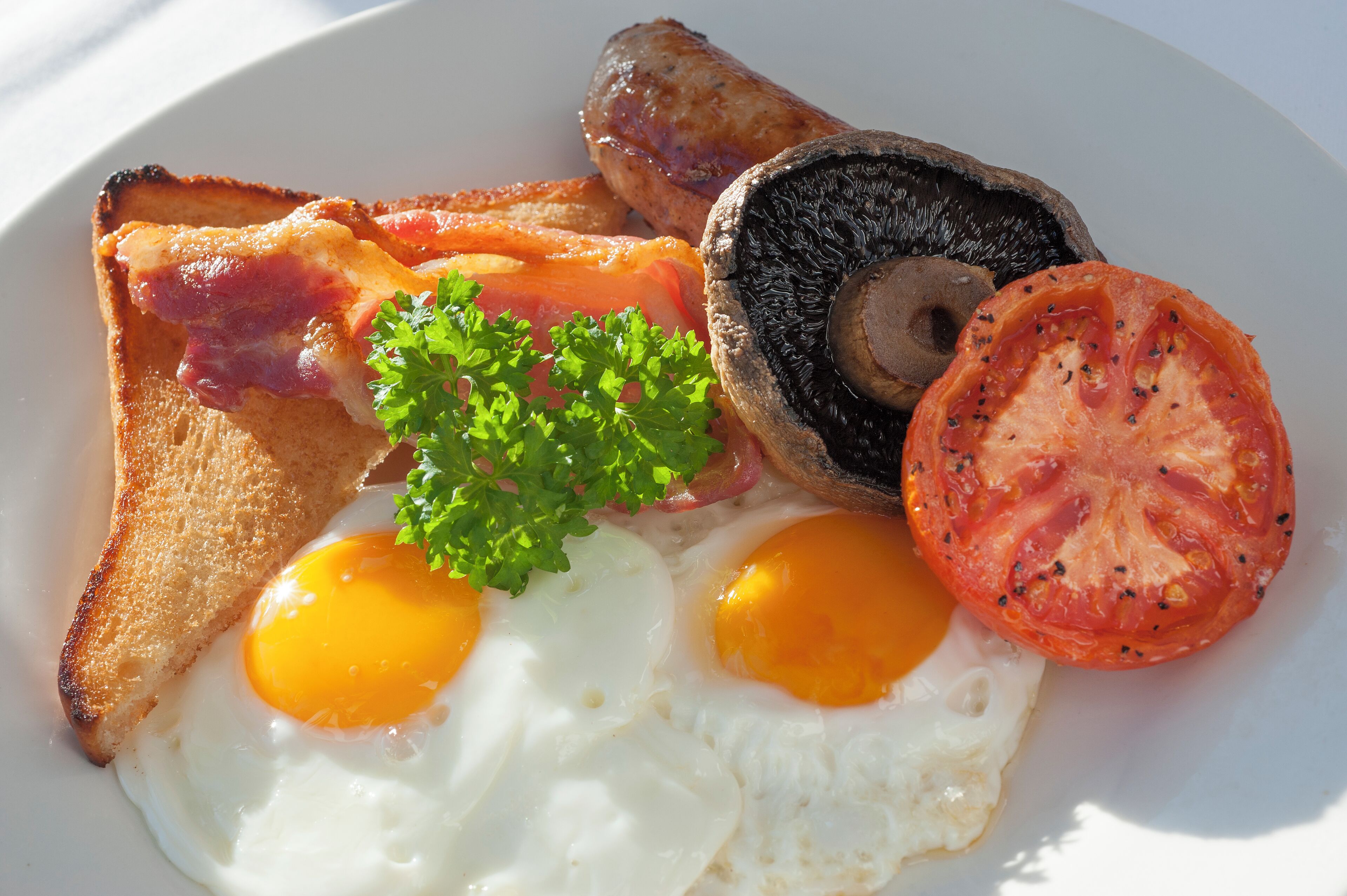 A plate with toast, eggs, sausages, mushrooms, and a tomato.