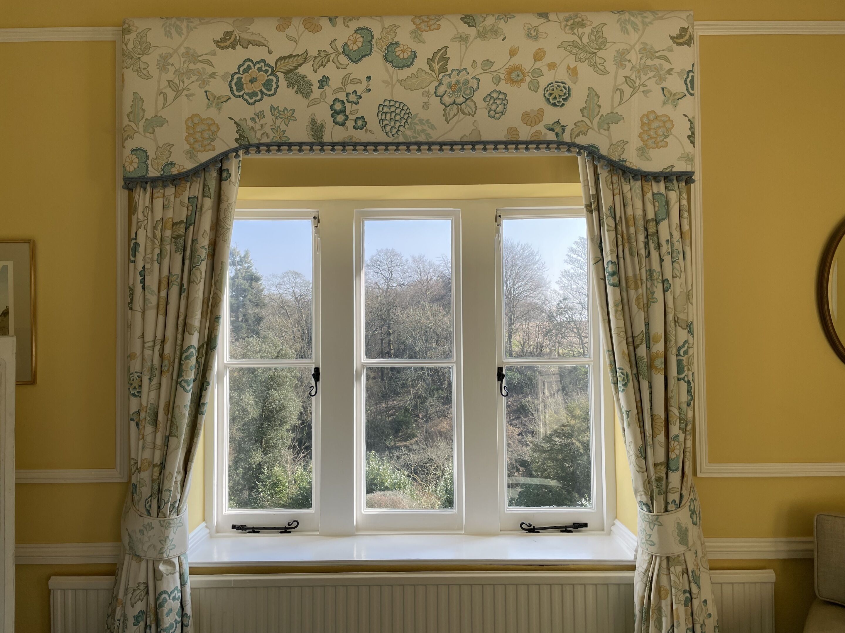 A room with a window featuring a floral curtain and a view of trees outside.