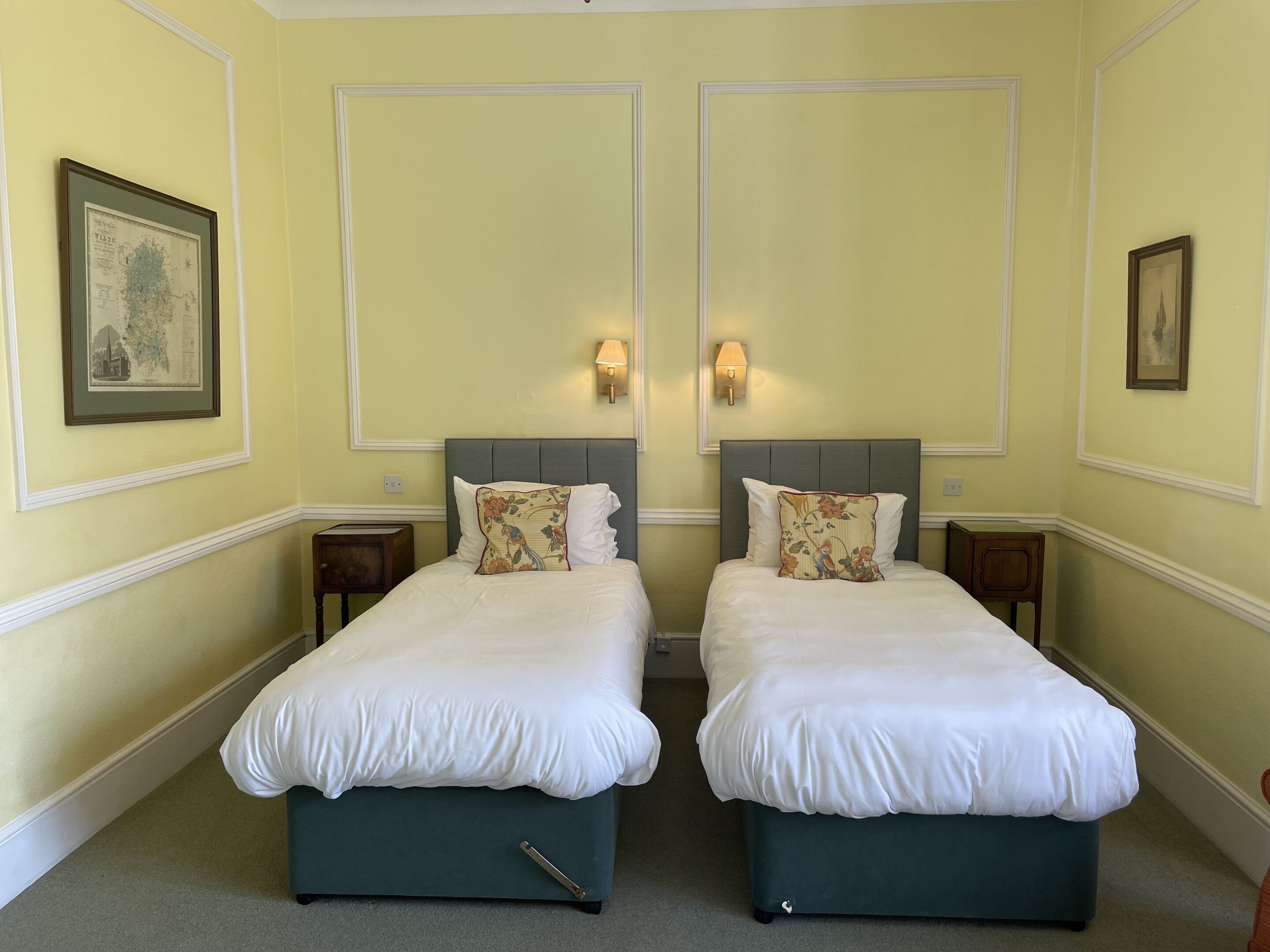 A room with two beds, each with a pillow and a nightstand.