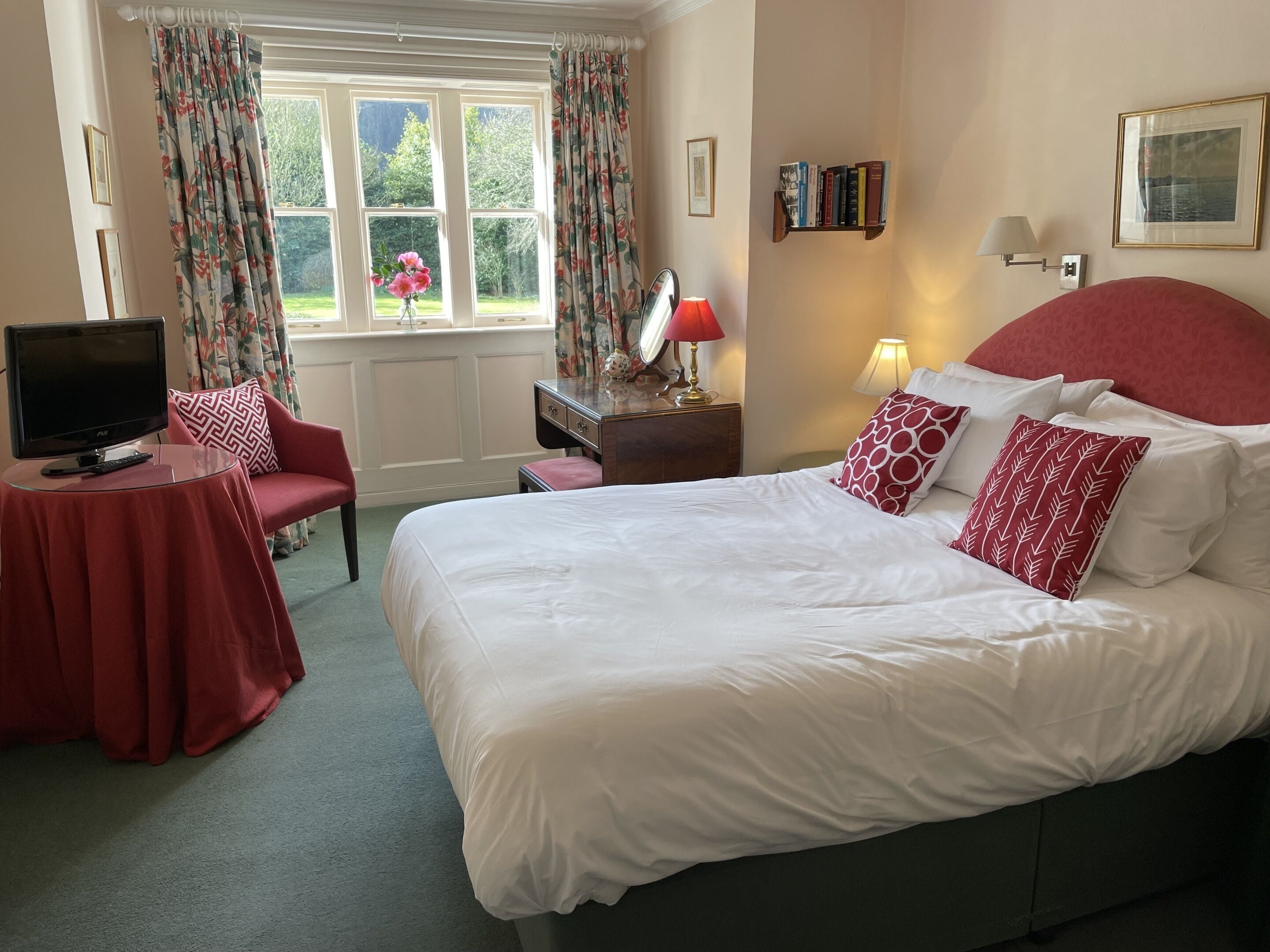 A hotel room with a large bed, a desk with a TV, a chair, and a window with curtains.