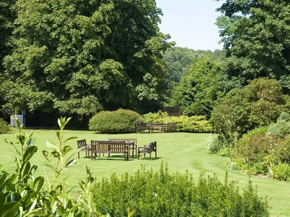 Un jardin bien entretenu, agrémenté d’un banc en bois et d’une table, entouré d’une végétation luxuriante et d’arbres.