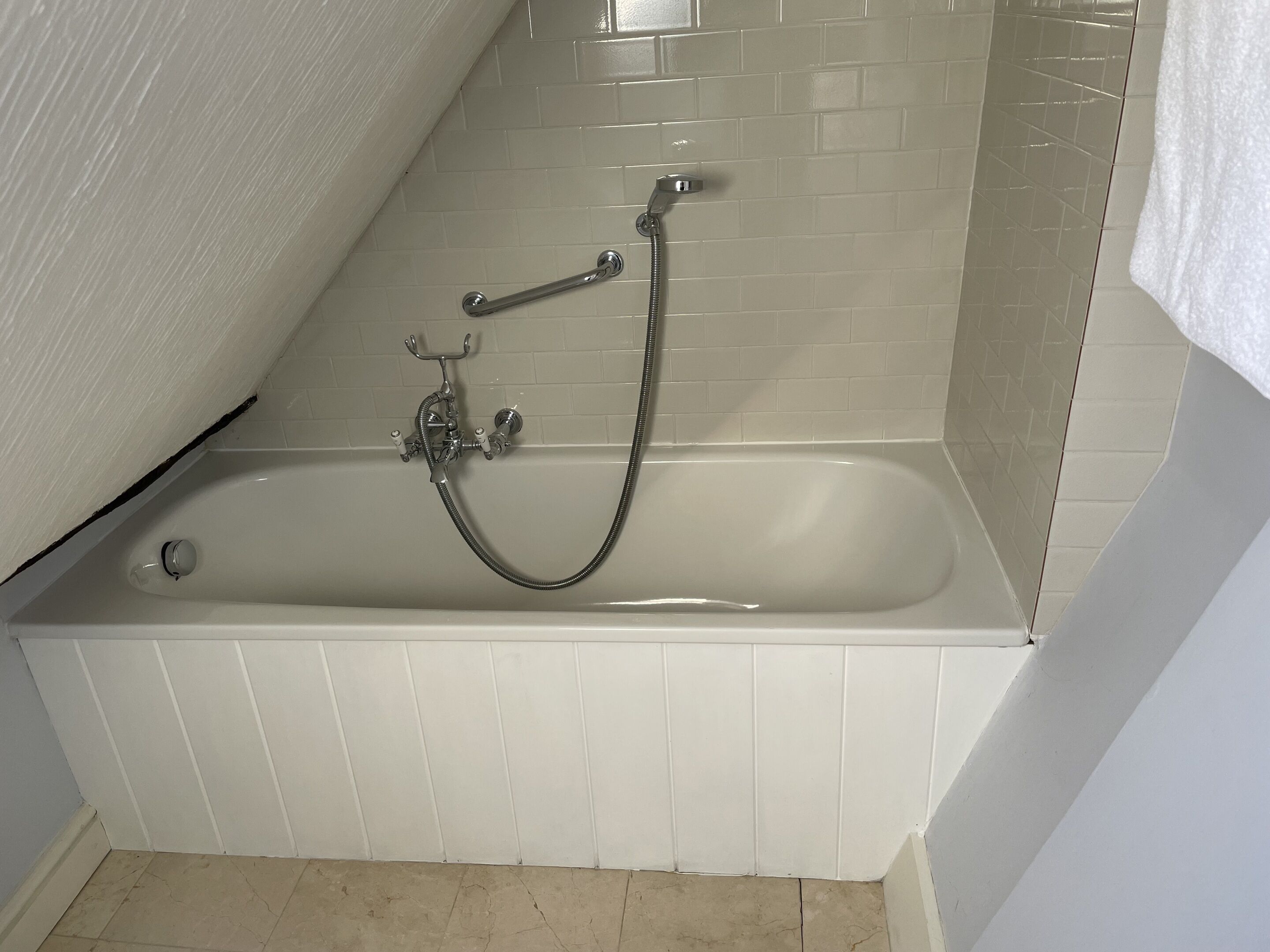 A bathroom with a bathtub, a handheld showerhead, and a wall-mounted faucet.