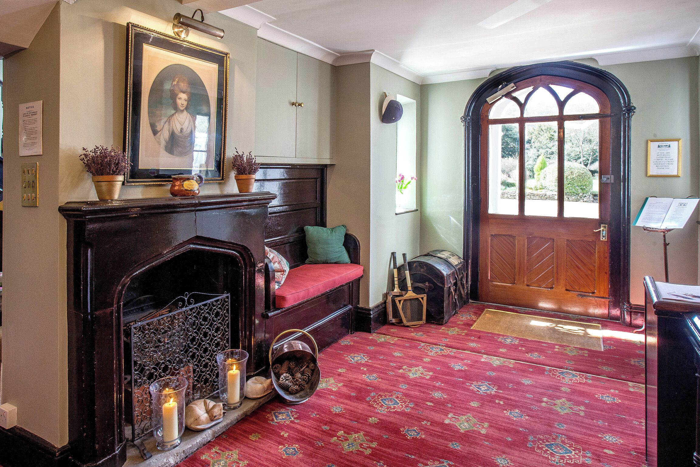 Quarto tradicional com lareira, tapete vermelho e porta de madeira com janela.