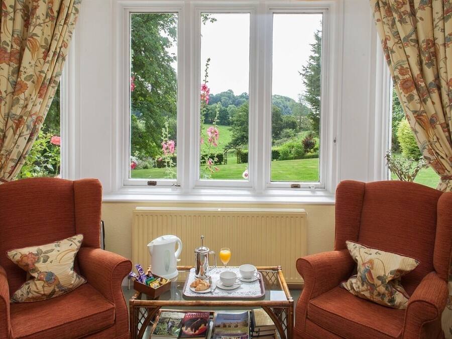 A room with two red armchairs, a small table with breakfast items, and a window with a view of a garden.