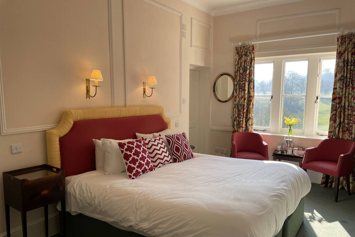A neatly arranged bedroom with a large bed, two bedside lamps, a mirror, and a window with curtains.