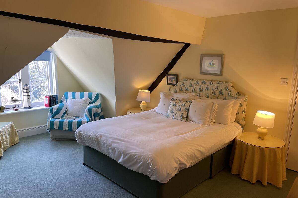 A bedroom with a large bed, a chair, two bedside tables, and a window with a view.