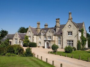 A large stone building with multiple chimneys, a well-maintained lawn, and a gravel driveway. - Langrish House (Petersfield)