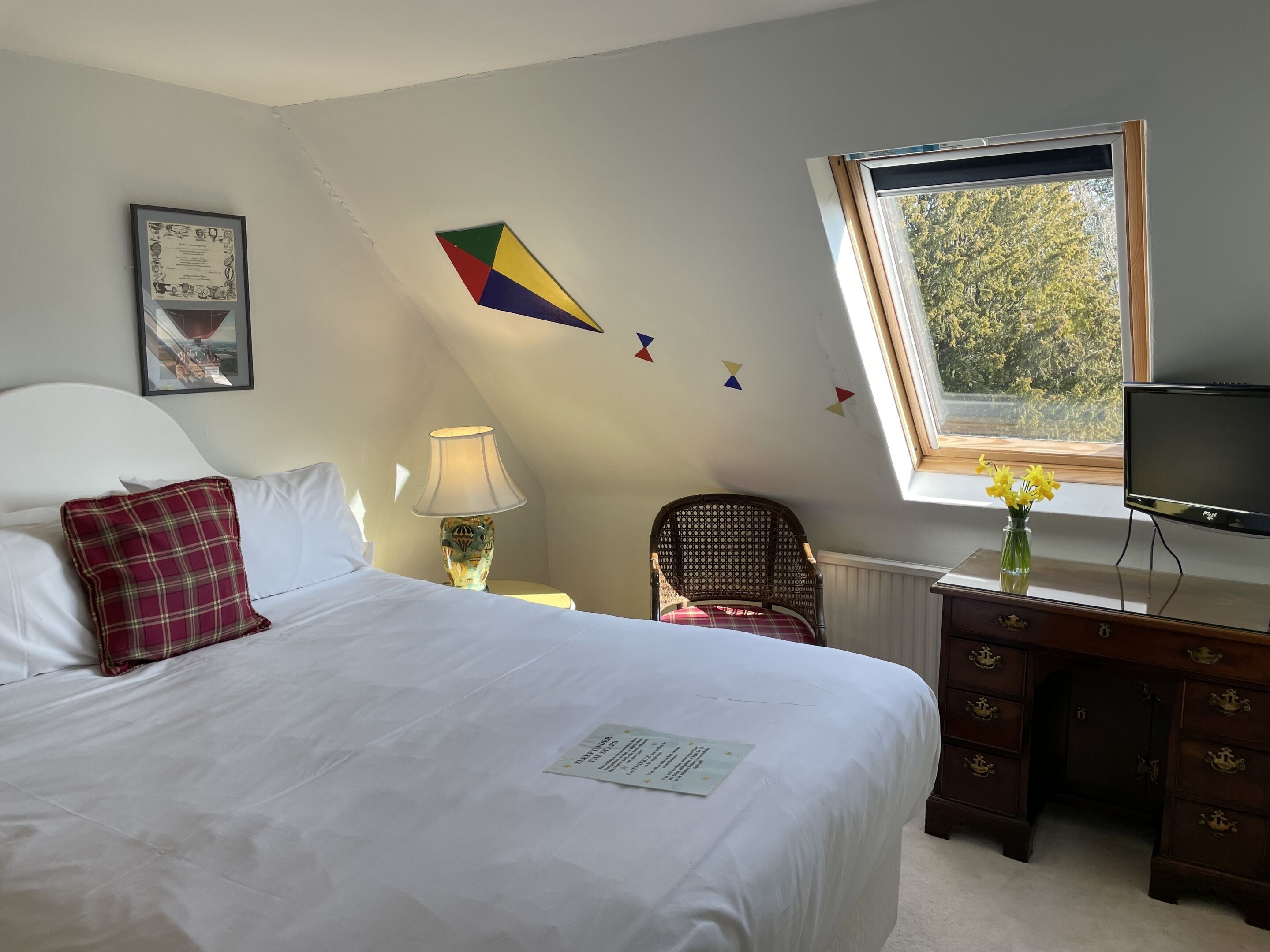 A bedroom with a bed, a desk, a chair, a lamp, a TV, a window with a view, and a certificate on the bed.