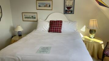 Uma cama bem arrumada com um travesseiro xadrez vermelho, um certificado emoldurado na parede e uma luminária em uma mesa de cabeceira.
