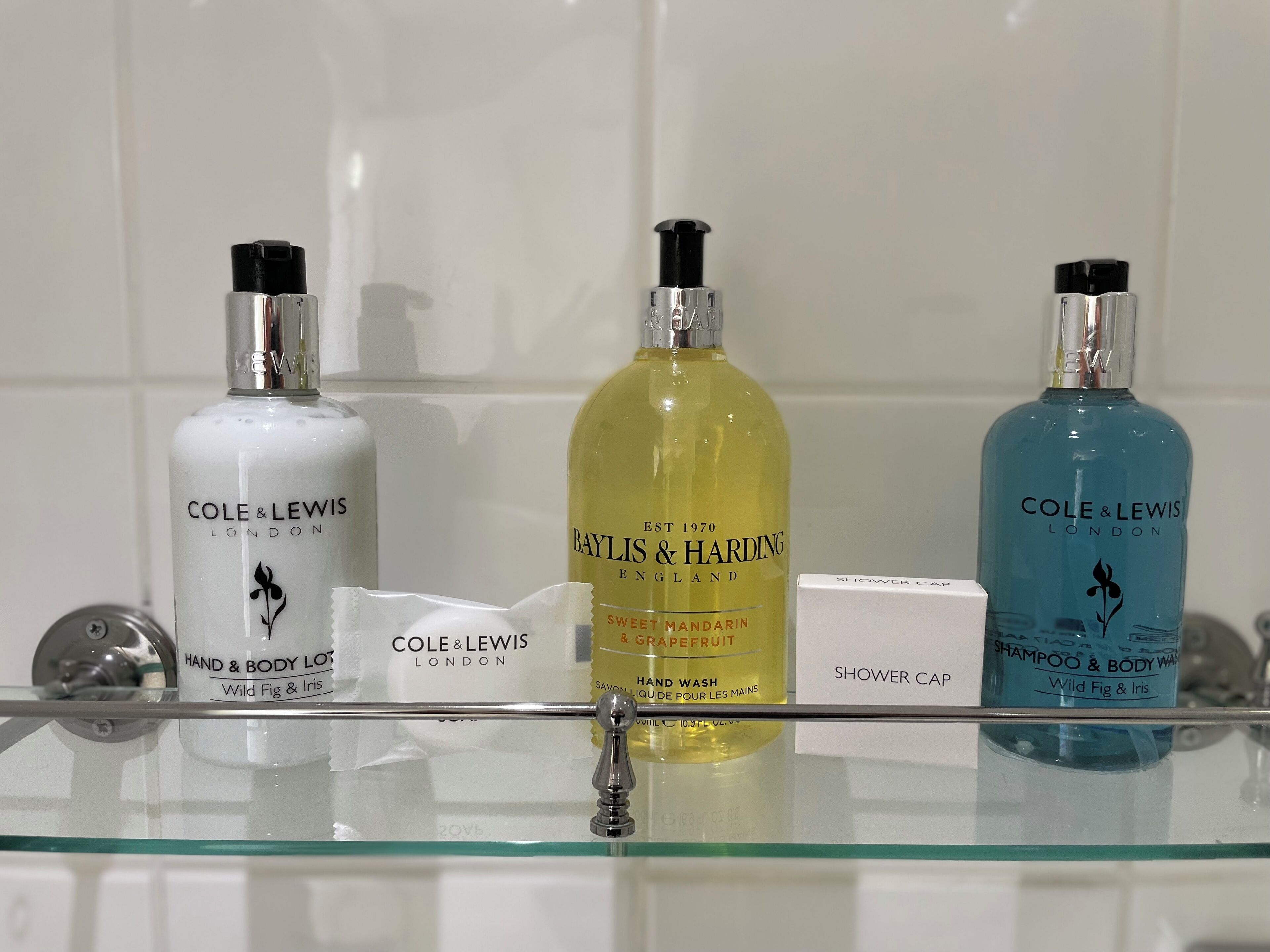 Tres botellas de jabón para manos y cuerpo sobre una repisa de vidrio en un baño.