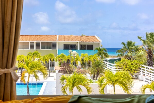Ein Hotelzimmer mit Blick auf einen Pool, Palmen und ein Gebäude mit einem Ziegeldach.